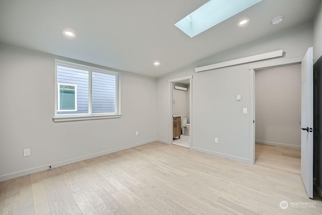 unfurnished bedroom featuring vaulted ceiling with skylight, ensuite bathroom, light hardwood / wood-style floors, and a wall mounted AC