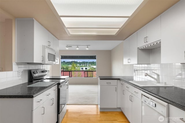 908 E Bay Dr NE Unit 203, Olympia, WA 98506 - kitchen featuring white appliances, a sink, light wood-style floors, dark countertops, and backsplash