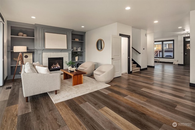 living room featuring dark hardwood / wood-style flooring, built in features, and a tiled fireplace