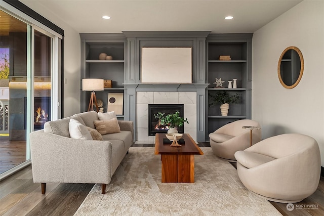 sitting room with a tile fireplace, built in shelves, and hardwood / wood-style flooring