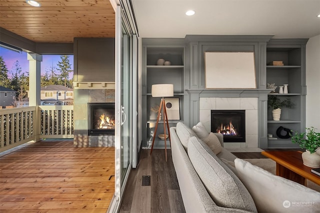 living room with wood-type flooring, built in features, wood ceiling, and a tiled fireplace