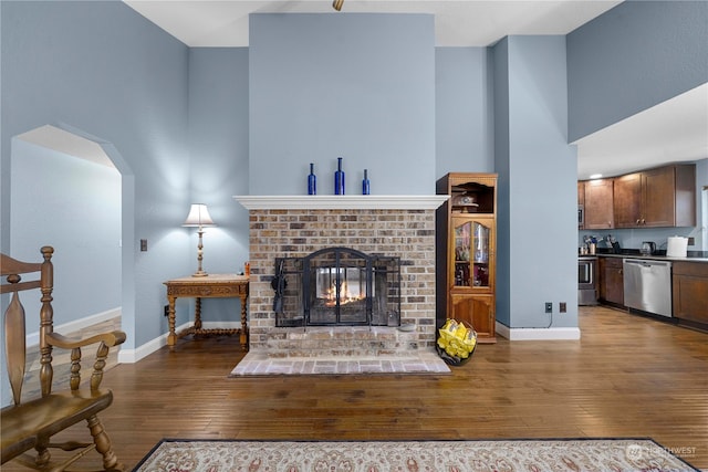 living room featuring wood-type flooring, a towering ceiling, and a brick fireplace