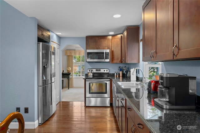 kitchen with hardwood / wood-style floors, sink, stainless steel appliances, and dark stone counters