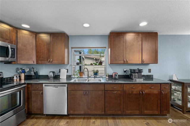 kitchen with wood-type flooring, stainless steel appliances, dark stone countertops, and sink