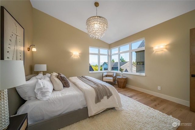 bedroom featuring light wood-type flooring, lofted ceiling, and a notable chandelier