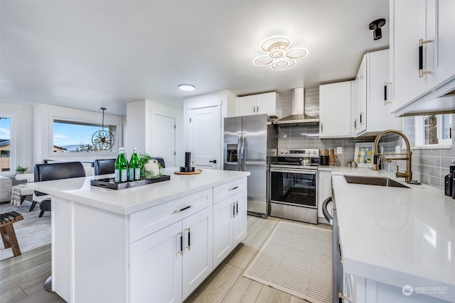 kitchen featuring pendant lighting, a center island, white cabinets, wall chimney exhaust hood, and appliances with stainless steel finishes