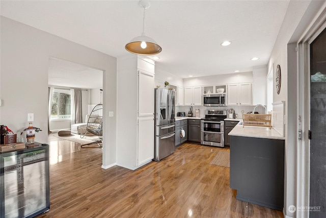 kitchen with gray cabinetry, stainless steel appliances, pendant lighting, white cabinets, and light wood-type flooring