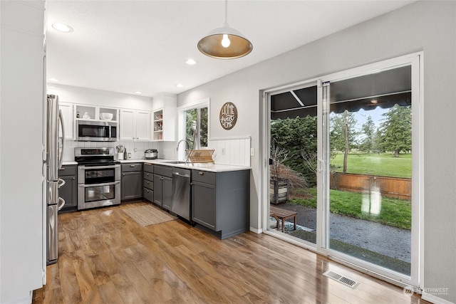 kitchen featuring gray cabinetry, light hardwood / wood-style flooring, decorative backsplash, decorative light fixtures, and stainless steel appliances