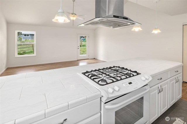 kitchen featuring tile countertops, white gas range, a wealth of natural light, island exhaust hood, and white cabinets