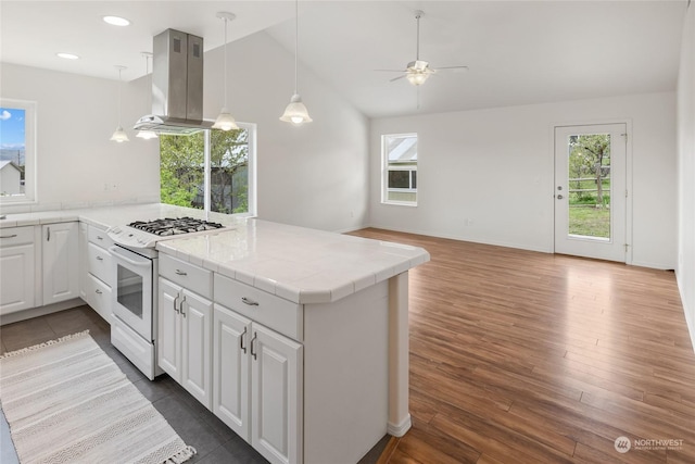 kitchen with white range with gas stovetop, white cabinetry, decorative light fixtures, kitchen peninsula, and island exhaust hood