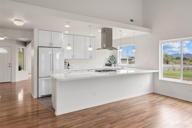 kitchen with hardwood / wood-style floors, white cabinetry, hanging light fixtures, island exhaust hood, and white appliances