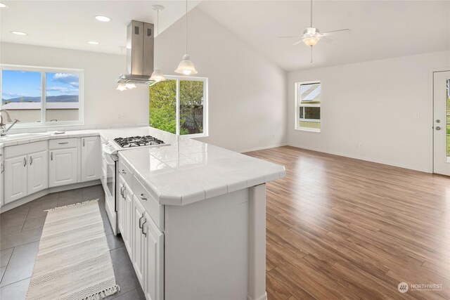 kitchen with white cabinets, hanging light fixtures, island exhaust hood, tile counters, and white range with gas stovetop