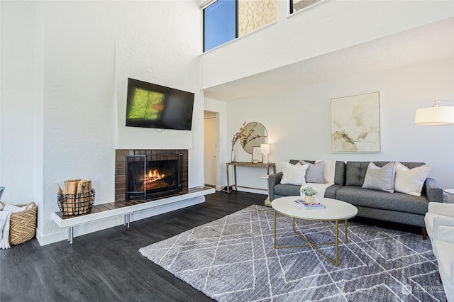 living room with a tile fireplace, a high ceiling, and dark hardwood / wood-style floors