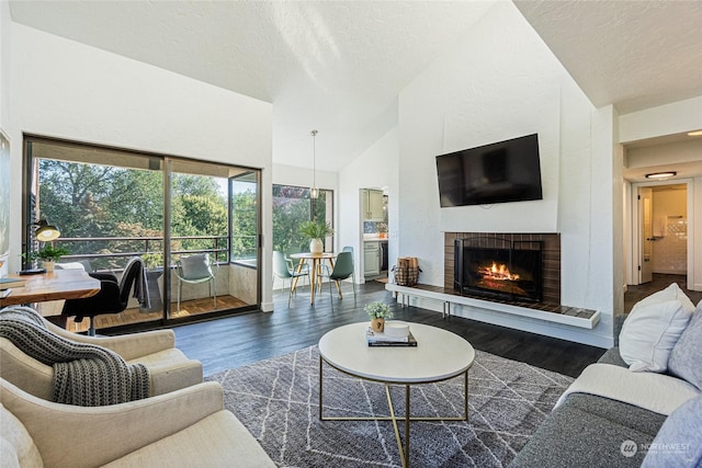 living room with a textured ceiling, dark hardwood / wood-style floors, vaulted ceiling, and a tiled fireplace