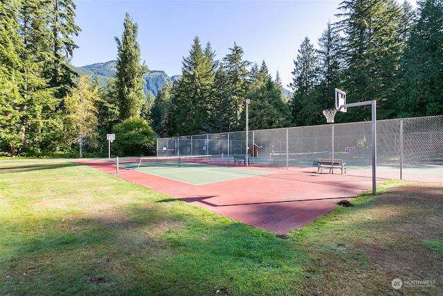 view of sport court featuring a mountain view, a lawn, and basketball hoop