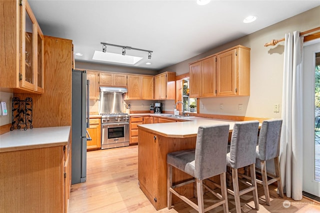 kitchen with a breakfast bar, sink, light hardwood / wood-style flooring, kitchen peninsula, and stainless steel appliances