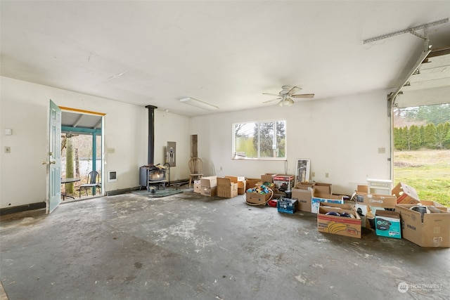 interior space featuring ceiling fan, concrete flooring, electric panel, and a wood stove