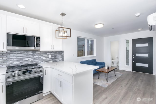 kitchen featuring light stone countertops, kitchen peninsula, stainless steel appliances, white cabinets, and hanging light fixtures