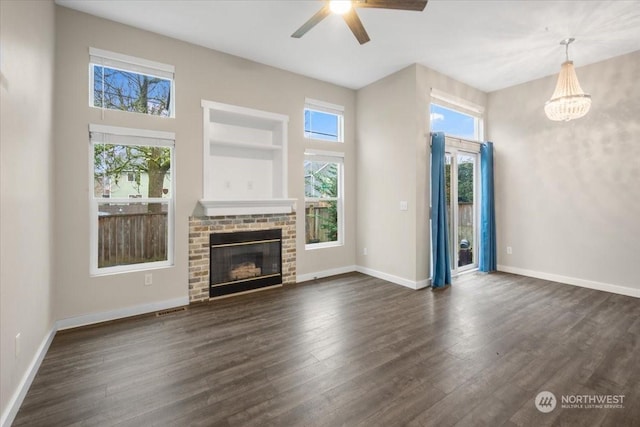 unfurnished living room featuring built in features, a brick fireplace, dark hardwood / wood-style flooring, and ceiling fan with notable chandelier