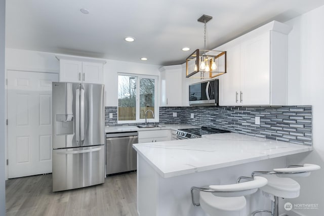 kitchen featuring kitchen peninsula, white cabinets, decorative light fixtures, and appliances with stainless steel finishes