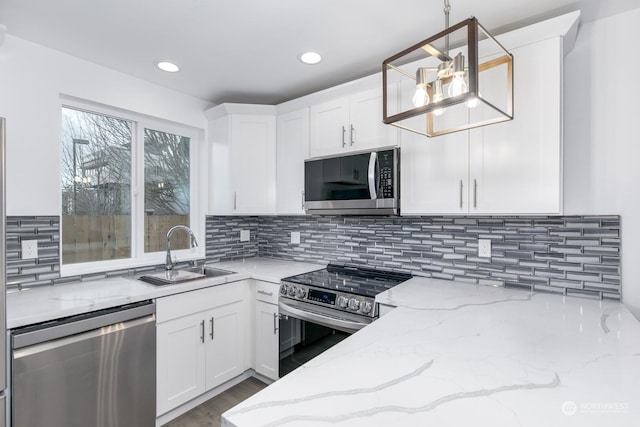 kitchen with light stone countertops, stainless steel appliances, sink, decorative light fixtures, and white cabinetry