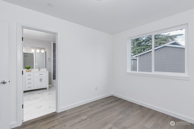 unfurnished bedroom with ensuite bathroom, light wood-type flooring, and sink