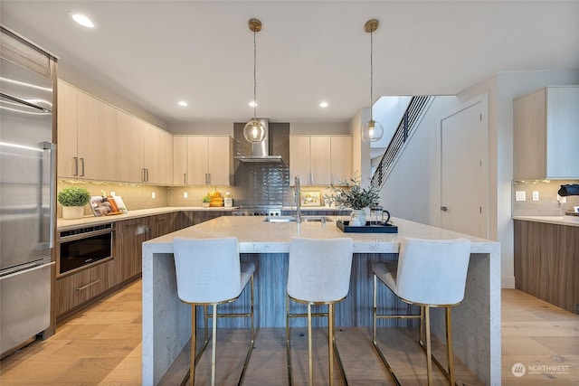 kitchen with a kitchen island with sink, pendant lighting, wall chimney range hood, and appliances with stainless steel finishes