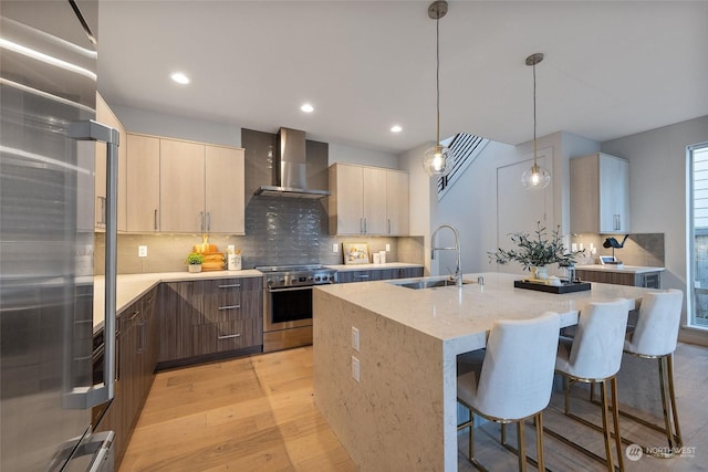 kitchen featuring wall chimney exhaust hood, stainless steel range, sink, pendant lighting, and light hardwood / wood-style flooring