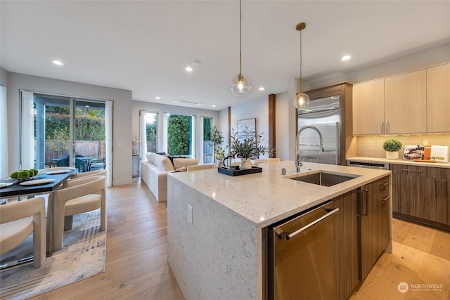 kitchen with light stone countertops, appliances with stainless steel finishes, sink, hanging light fixtures, and an island with sink