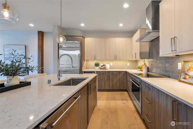 kitchen with hanging light fixtures, sink, stainless steel appliances, and wall chimney range hood