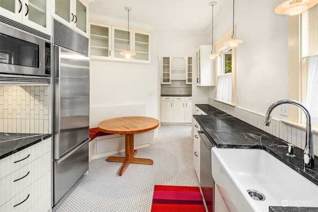 kitchen with appliances with stainless steel finishes, sink, white cabinets, backsplash, and hanging light fixtures