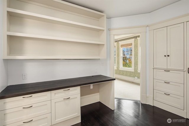 unfurnished office featuring dark hardwood / wood-style flooring and built in desk