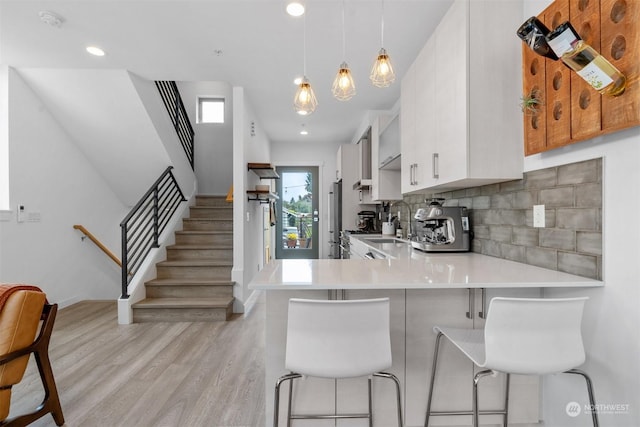 kitchen with pendant lighting, backsplash, white cabinets, a kitchen breakfast bar, and kitchen peninsula