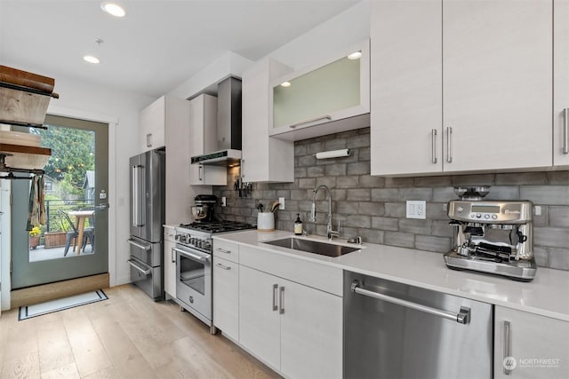 kitchen featuring sink, wall chimney range hood, backsplash, white cabinets, and appliances with stainless steel finishes