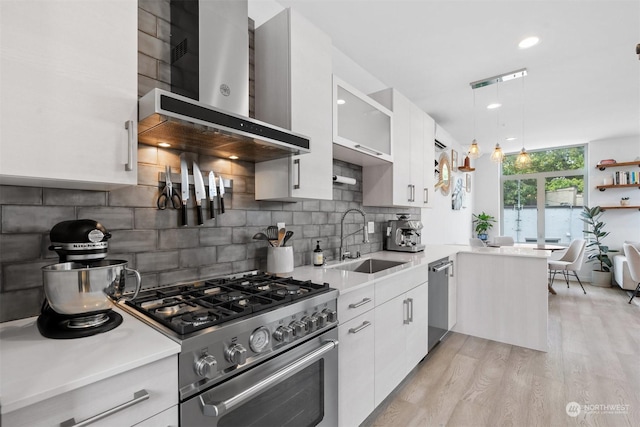 kitchen with white cabinets, wall chimney exhaust hood, stainless steel appliances, and decorative light fixtures