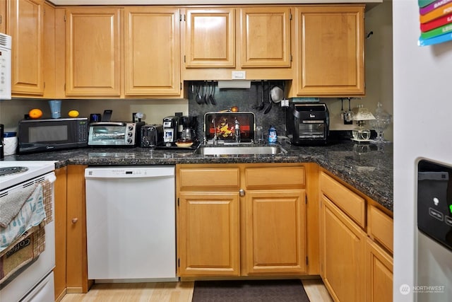 kitchen with white appliances, dark stone counters, and sink