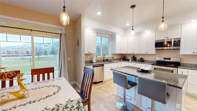 kitchen with appliances with stainless steel finishes, dark stone counters, a kitchen island, decorative light fixtures, and white cabinetry