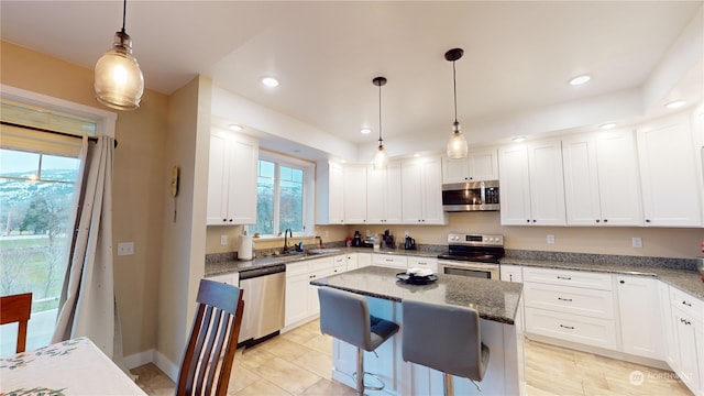 kitchen featuring white cabinets, appliances with stainless steel finishes, decorative light fixtures, and a kitchen island