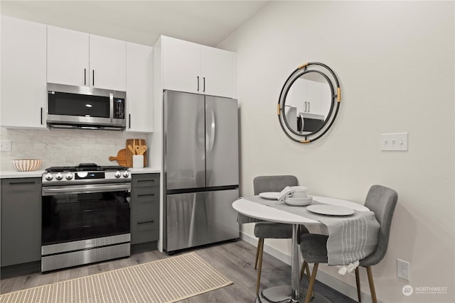 kitchen featuring lofted ceiling, tasteful backsplash, wood-type flooring, stainless steel appliances, and white cabinets