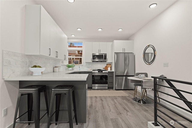 kitchen with a breakfast bar area, light wood-type flooring, appliances with stainless steel finishes, kitchen peninsula, and white cabinets