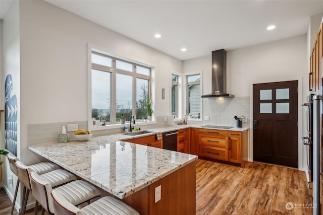 kitchen with light stone countertops, kitchen peninsula, wall chimney exhaust hood, and a breakfast bar area