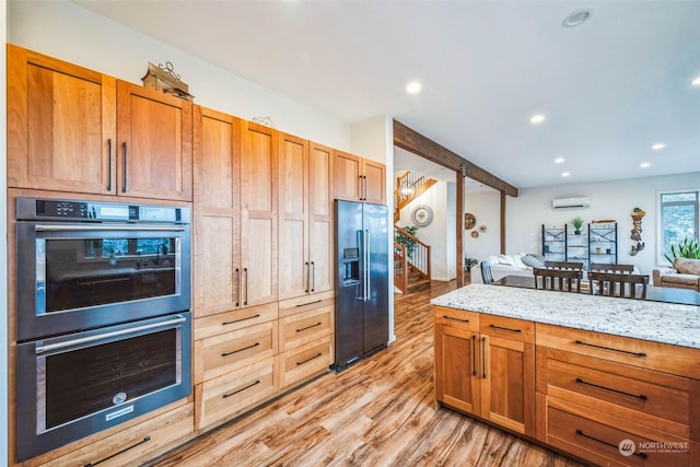 kitchen with a wall mounted AC, double wall oven, high quality fridge, light hardwood / wood-style flooring, and light stone counters