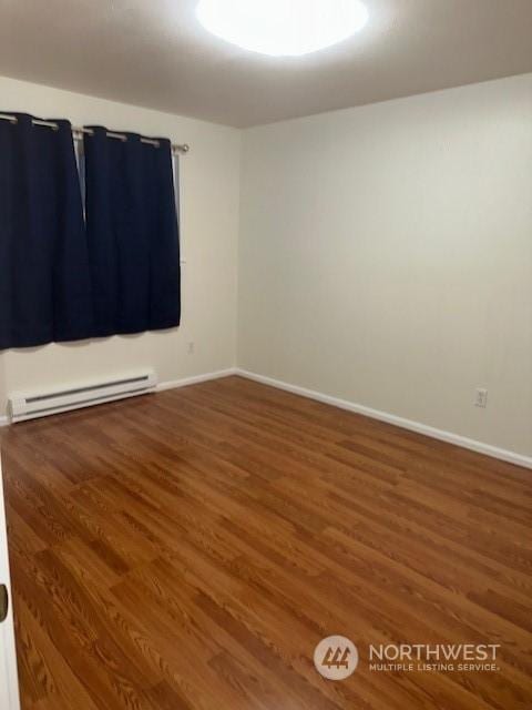 spare room featuring baseboard heating and dark hardwood / wood-style floors