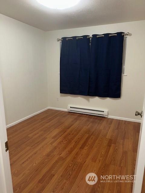 unfurnished room with hardwood / wood-style floors and a baseboard radiator