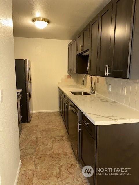 kitchen featuring light stone countertops, dark brown cabinetry, sink, and appliances with stainless steel finishes