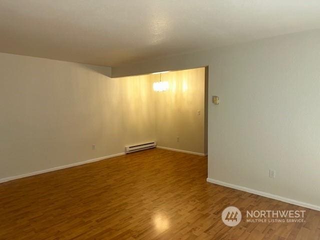 unfurnished room featuring hardwood / wood-style flooring, an inviting chandelier, and a baseboard heating unit