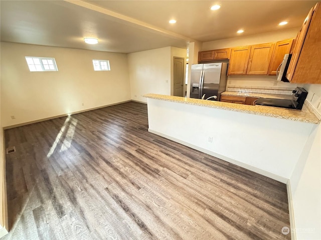 kitchen with dark hardwood / wood-style floors, light stone countertops, kitchen peninsula, and appliances with stainless steel finishes