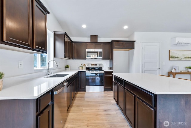 kitchen featuring a sink, an AC wall unit, light countertops, light wood-style floors, and appliances with stainless steel finishes