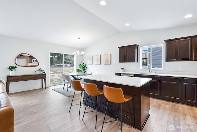 kitchen with a kitchen island, a sink, light countertops, light wood-style floors, and decorative light fixtures