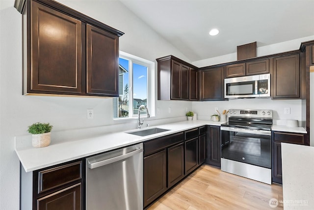 kitchen with appliances with stainless steel finishes, light countertops, a sink, dark brown cabinetry, and light wood finished floors